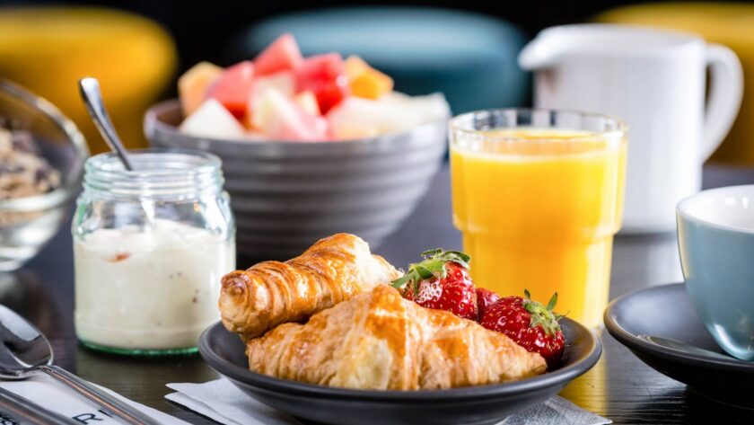 Delicious hotel breakfast with fresh croissants, strawberries, yoghurt, orange juice, and a colourful fruit bowl.