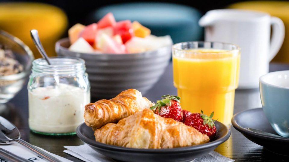 Delicious hotel breakfast with fresh croissants, strawberries, yoghurt, orange juice, and a colourful fruit bowl.