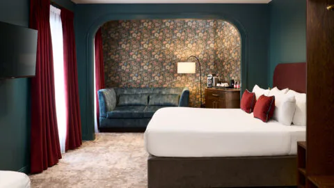 Elegant hotel room with plush bed, blue sofa, floral wallpaper, and modern amenities for a relaxing stay.