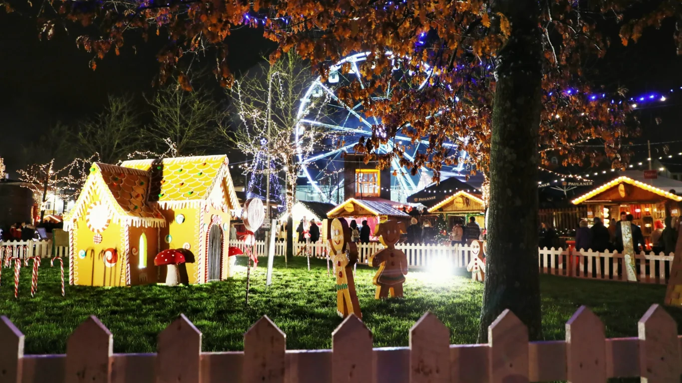 Festive Christmas market with a lit Ferris wheel and gingerbread house, surrounded by twinkling lights and vibrant stalls.