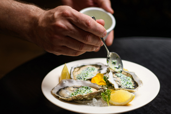 Fresh oysters on ice served with lemon wedges and herbs in a luxurious hotel dining setting.
