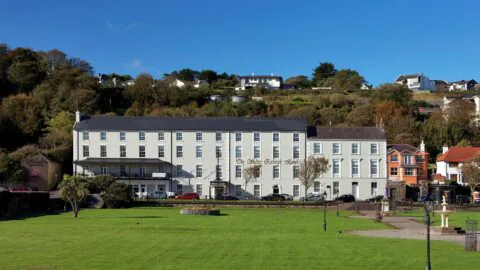Charming coastal hotel with lush gardens, hillside views, and elegant façade. Ideal for a tranquil holiday retreat.